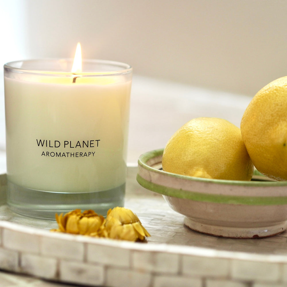 Lemon Verbena Aromatherapy Candle with flame on tray with bowl of fresh lemons and flowers