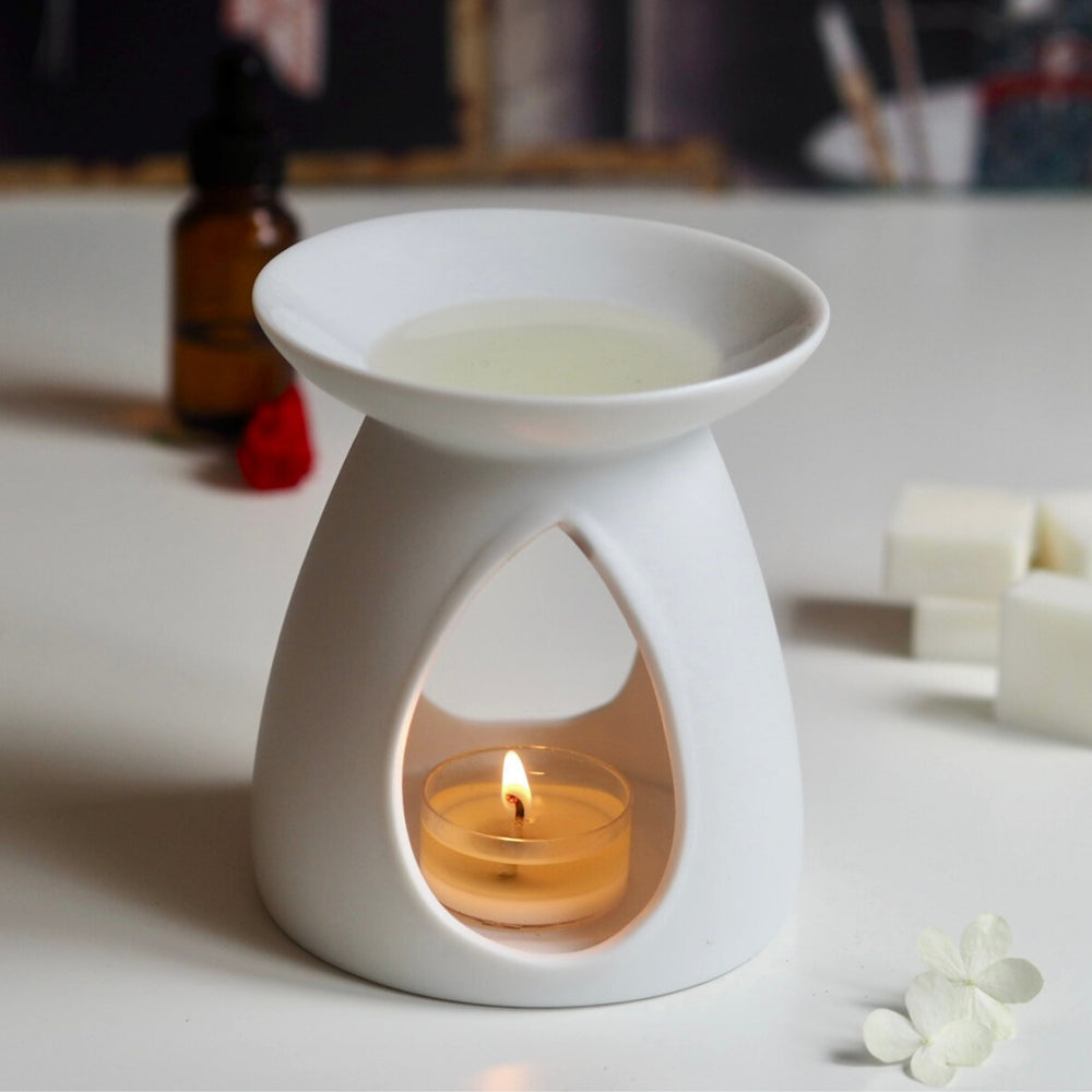 Hedonist Luxury Wax Melt in white ceramic oil burner, lit tea light on white table and amber bottle