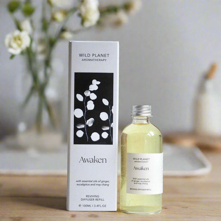 Awaken Natural Reed Diffuser Refill bottle and box by Wild Planet on wooden table with flowers