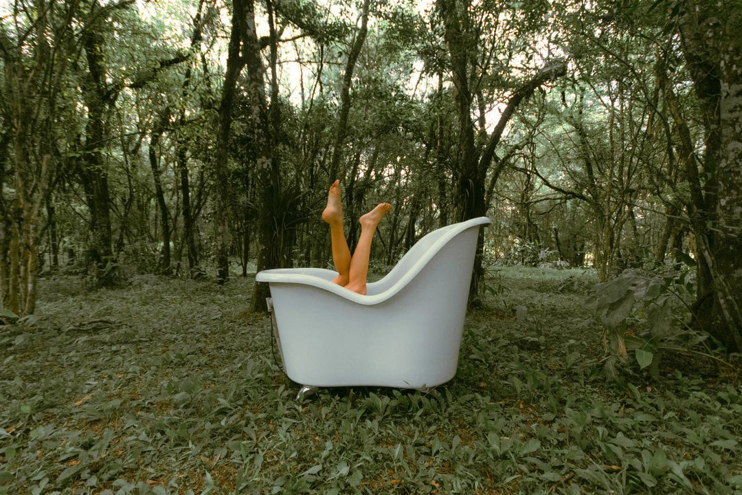 a white roll top bath with legs sticking out in the middle of a forest