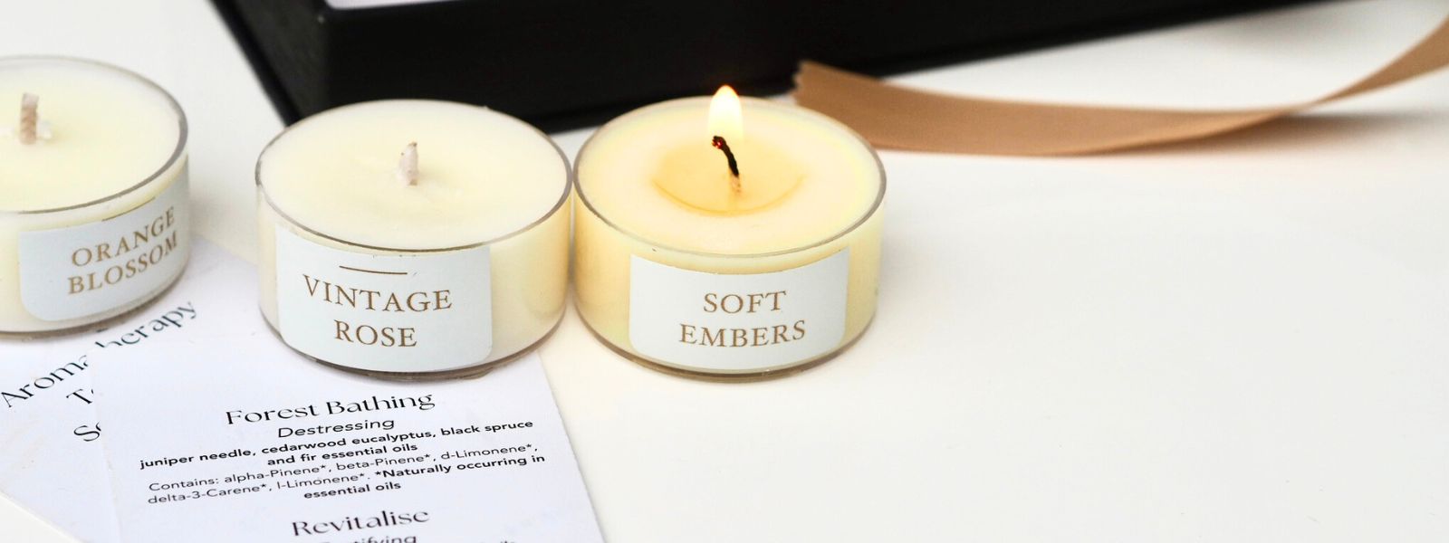 three tea lights, one with flame outside black box, ribbon and card by Wild Planet Aromatherapy