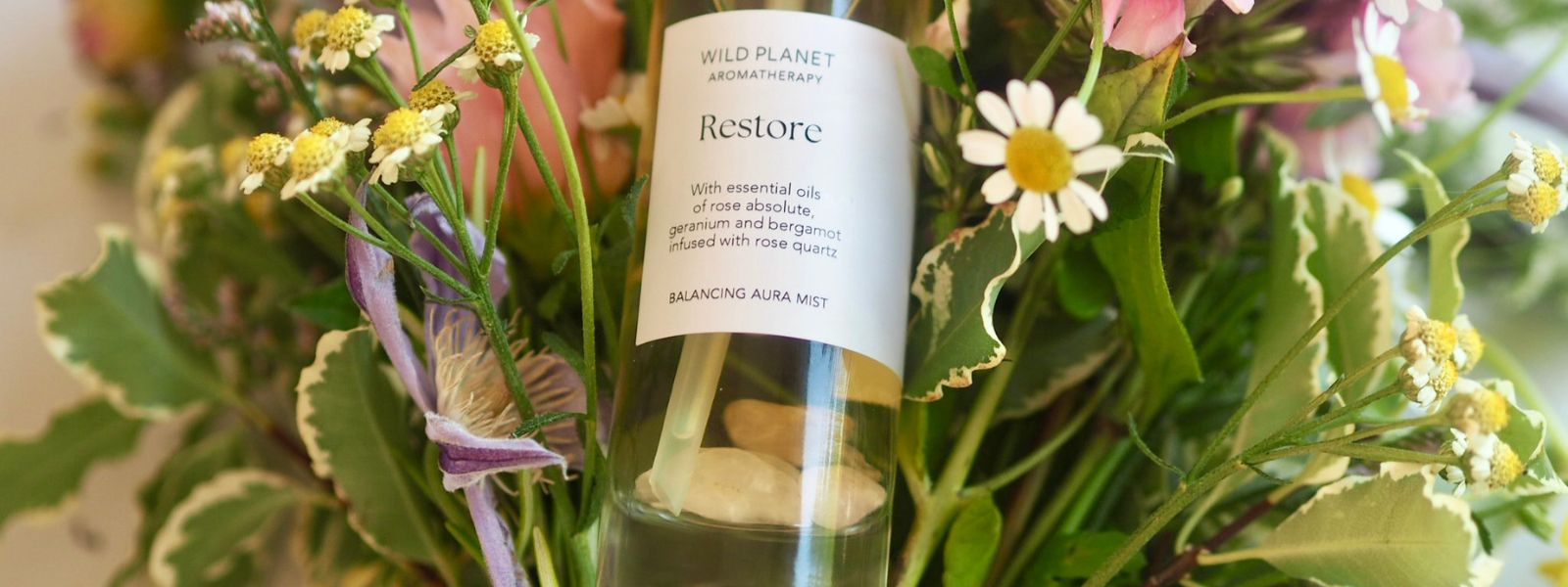 Restore Aura Mist lying on fresh summer flowers by Wild Planet Aromatherapy