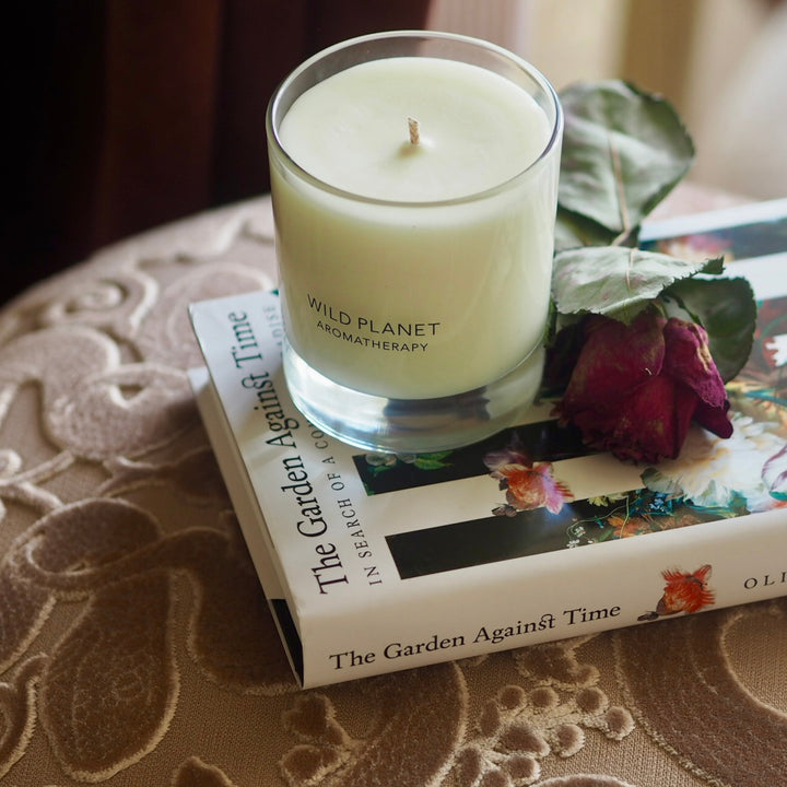 Wild Planet Aromatherapy candle placed on a book titled "The Garden Against Time" with a wilted rose