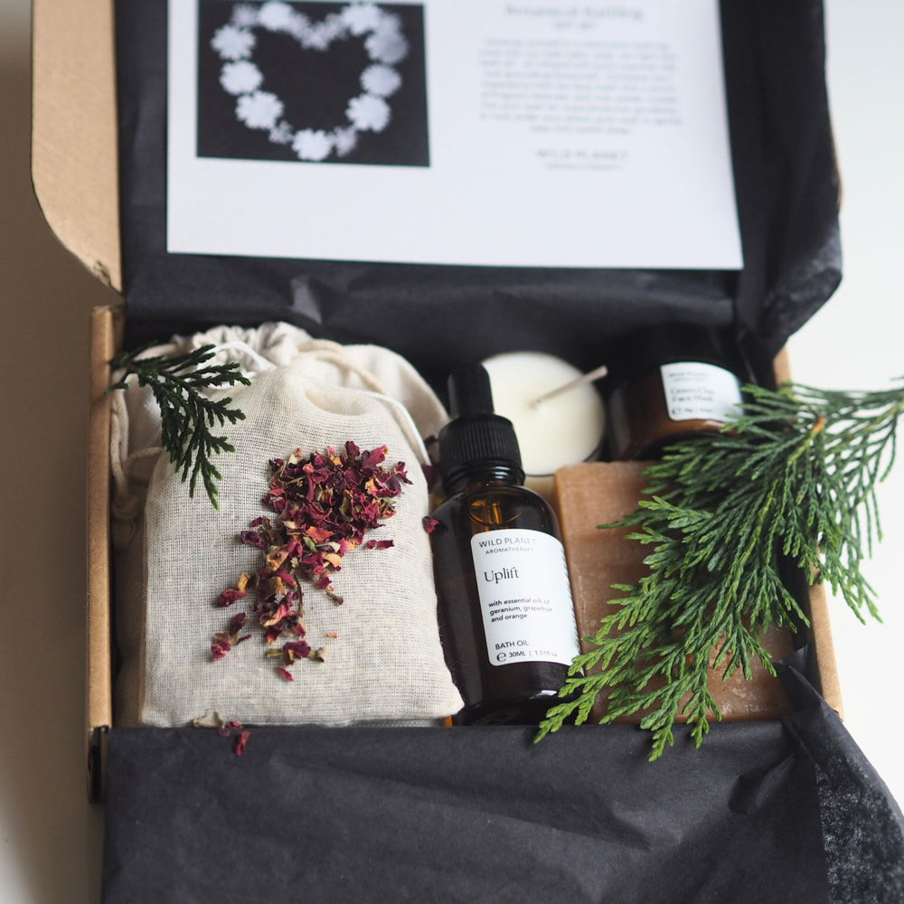 Lavender and roses in cotton bag, bath oil, soap bar, tea light in open box with green pine 