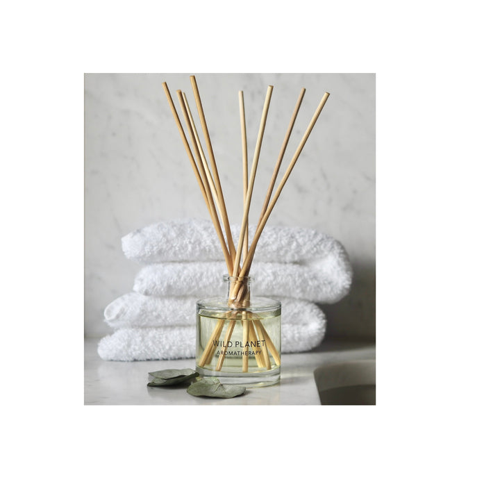 Wild Planet Aromatherapy reed diffuser in a glass bottle, set in front of stacked white towels.