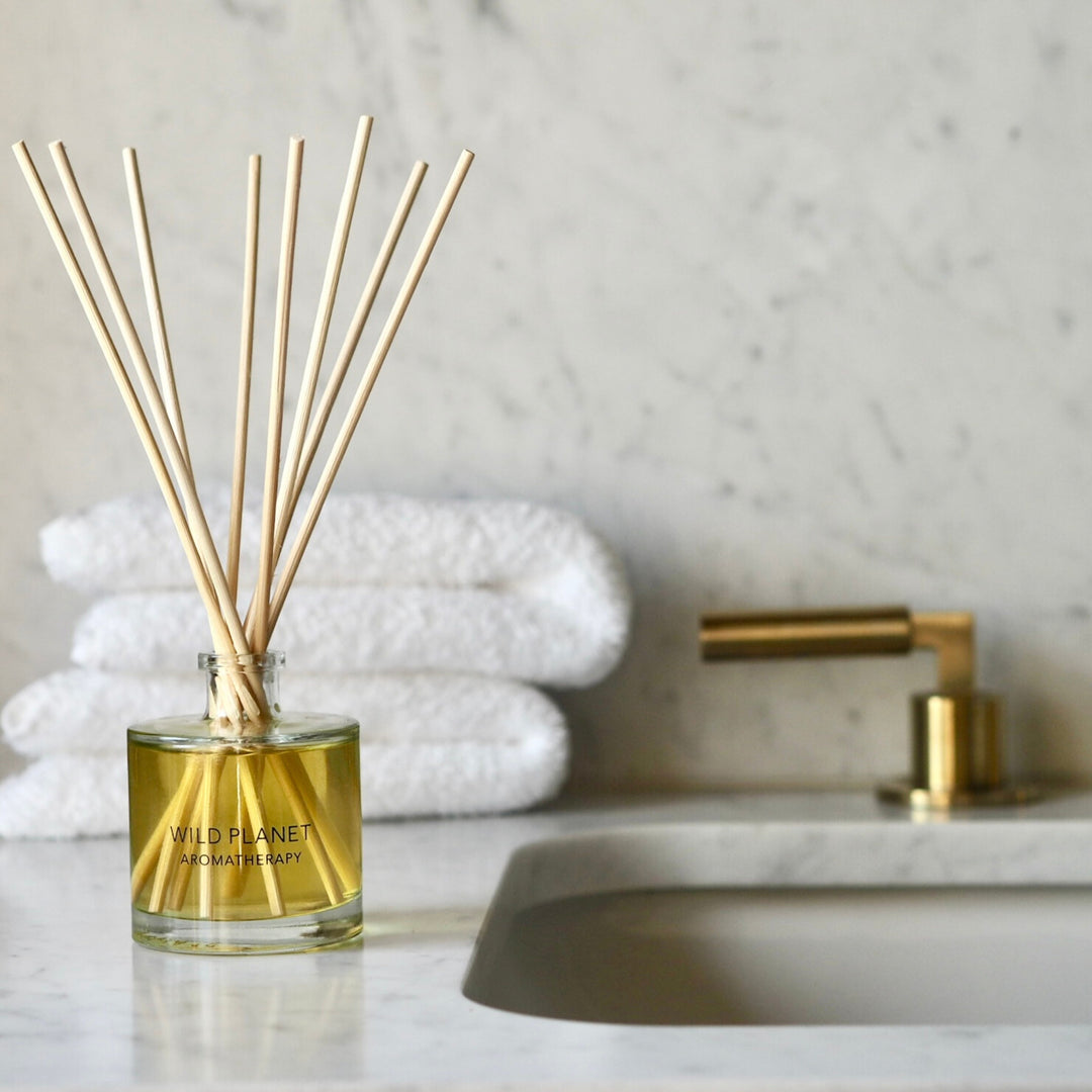 Wild Planet Aromatherapy natural reed diffuser placed on counter beside neatly stacked white towels.