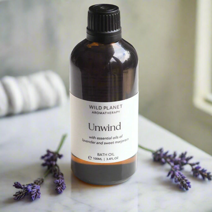 Unwind Natural Relaxing Lavender Bath Oil on marble surface with lavender flowers and towel