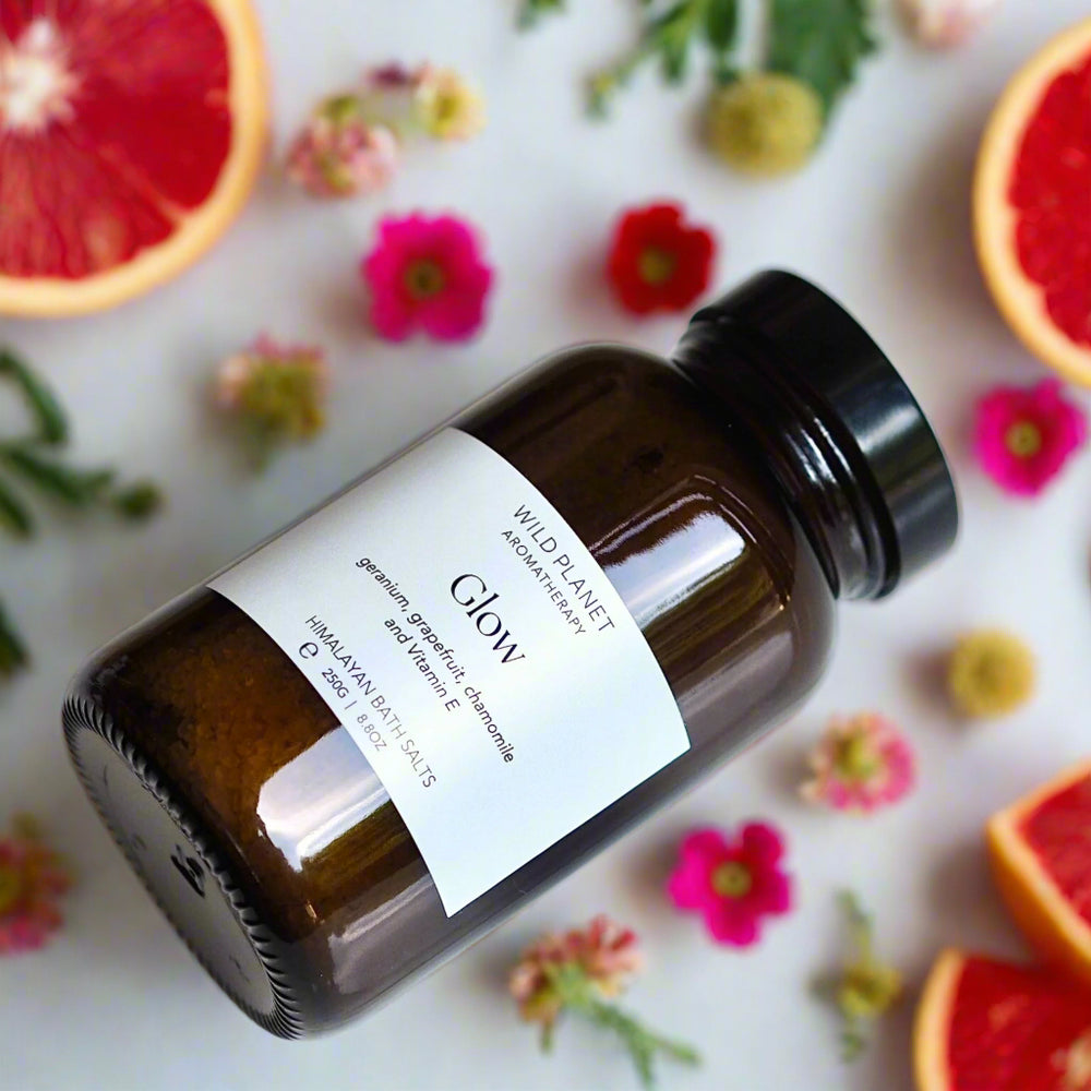 Glow Himalayan bath salts in amber glass jar on white background with  flowers leaves and grapefruit