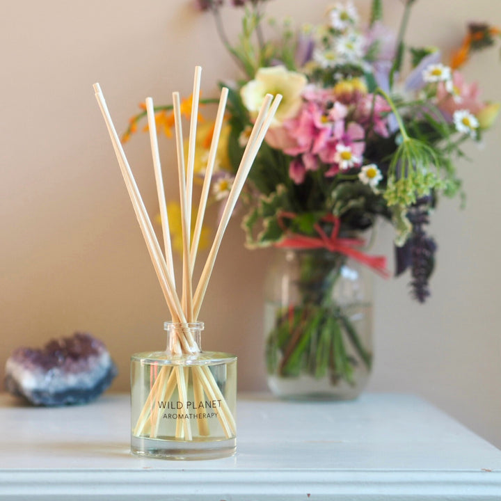 Wild Planet Aromatherapy natural reed diffuser with bouquet of wildflowers in the background.