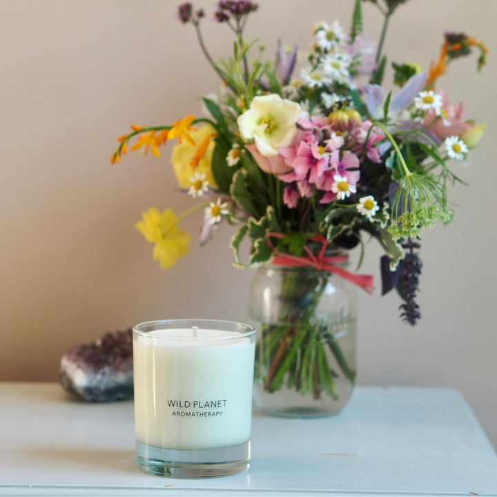 Wild Planet Aromatherapy relaxing vegan candle on a table next to a colourful freshly picked flowers