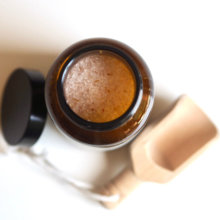 open amber glass jar of energising Himalayan bath salts with essential oils with wooden scoop