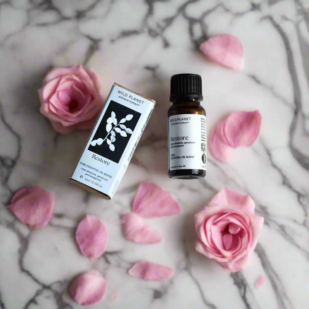 Restore essential oil blend amber bottle and box on grey marble top with pink roses