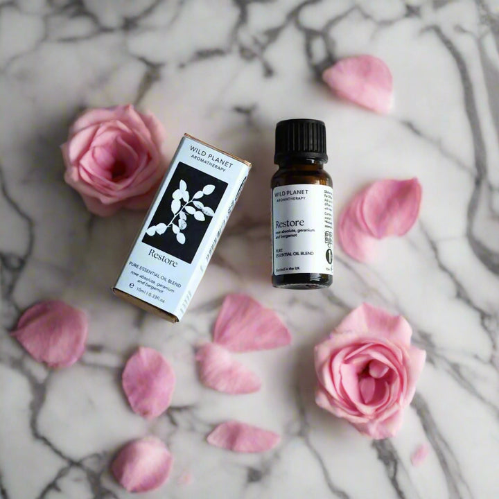 Restore essential oil blend amber bottle and box on grey marble top with pink roses