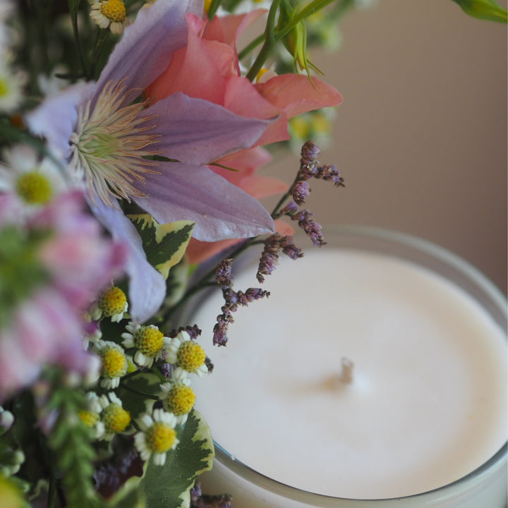 Close up of a Wild Planet Aromatherapy relaxing candle surrounded by purple & pick petals