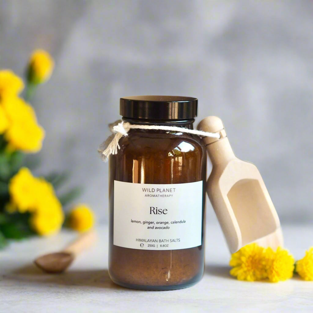 energising Himalayan bath salts with essential oils amber glass jar, wooden scoop, yellow flowers