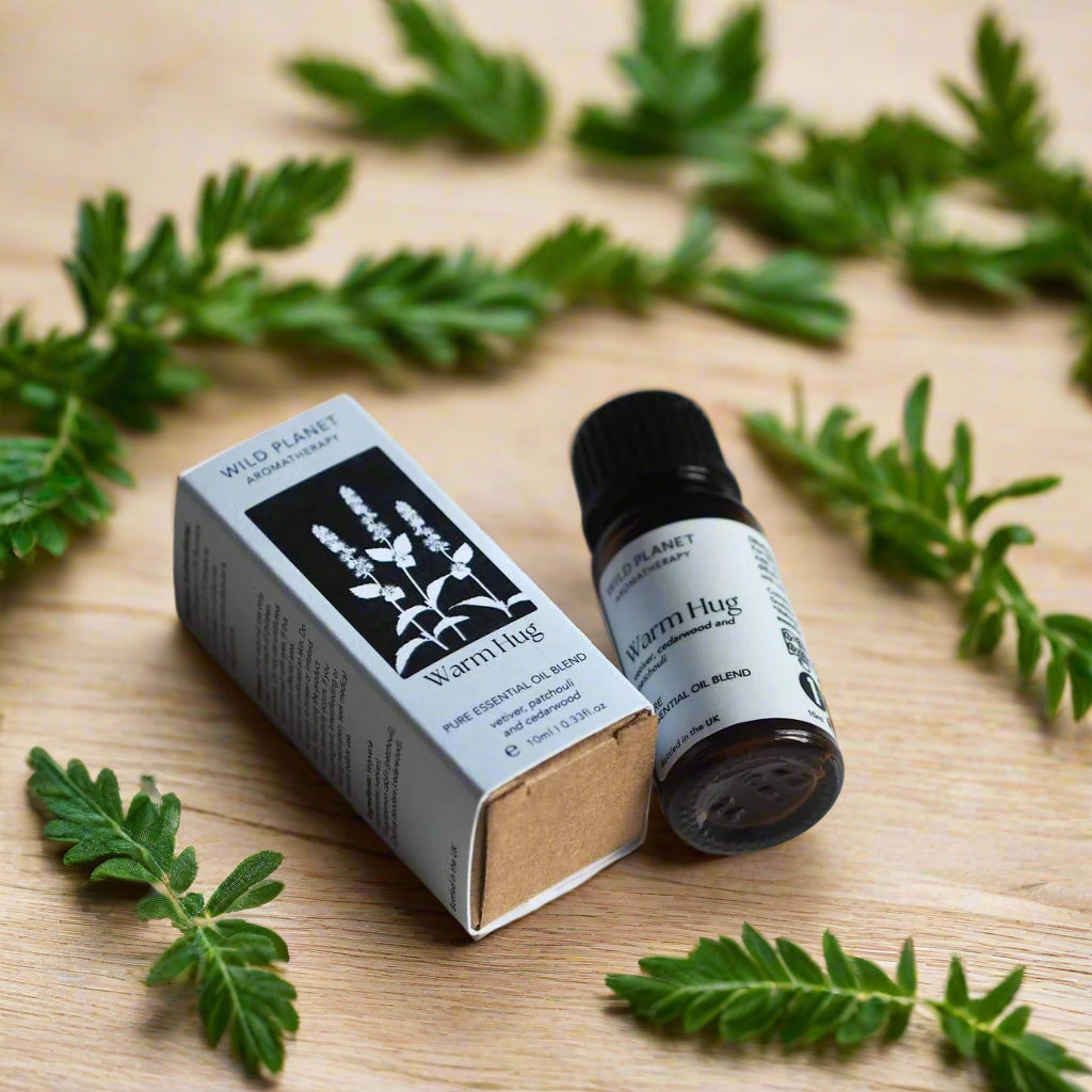 Warm Hug comforting essential oil blend bottle and box flat lay on wooden table with green leaves