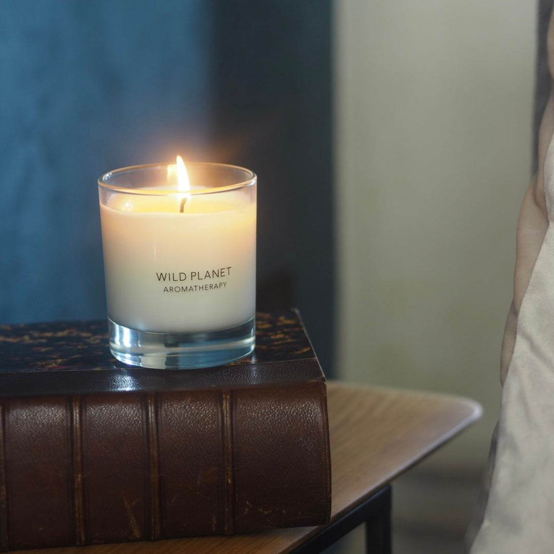 A lit Wild Planet Aromatherapy candle on two stacked leather bound books against blue background