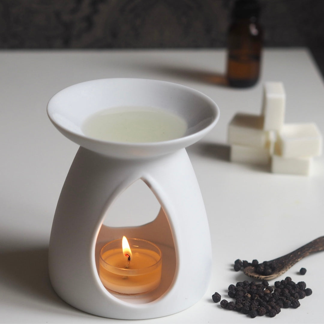 White ceramic oil burner with lit tea light heating Wild Planet luxury wax melt next to peppercorns.