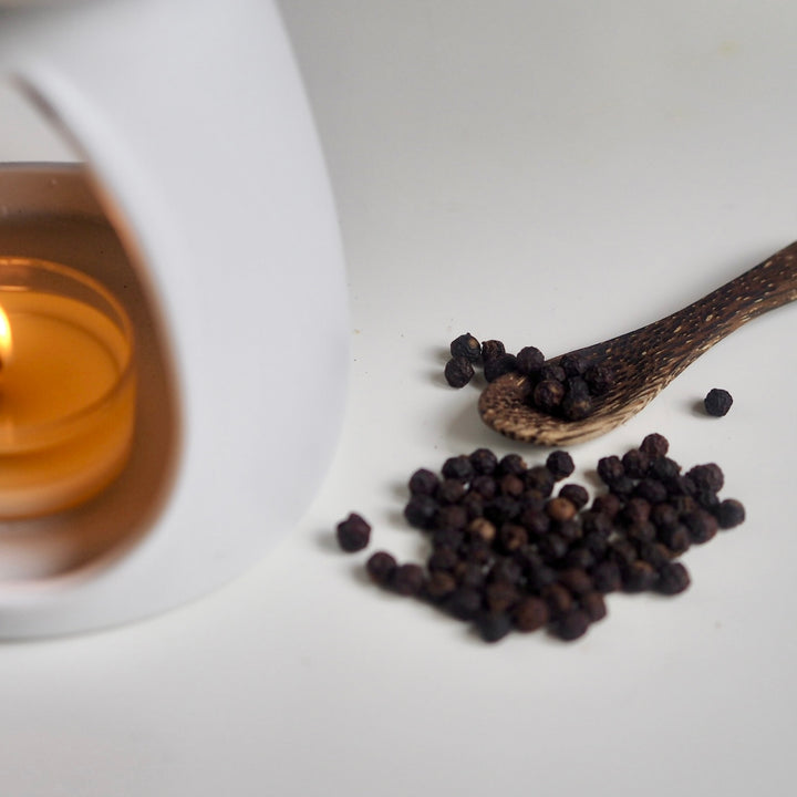 White ceramic oil burner with lit tea light heating Wild Planet luxury wax melt next to peppercorns.