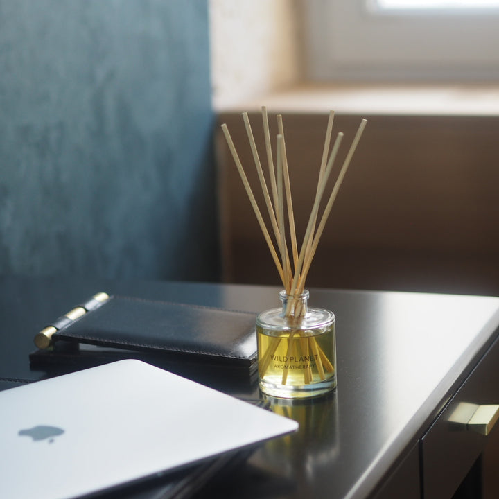 Wild Planet Aromatherapy natural reed diffuser on a desk next to laptop with a blurred background.