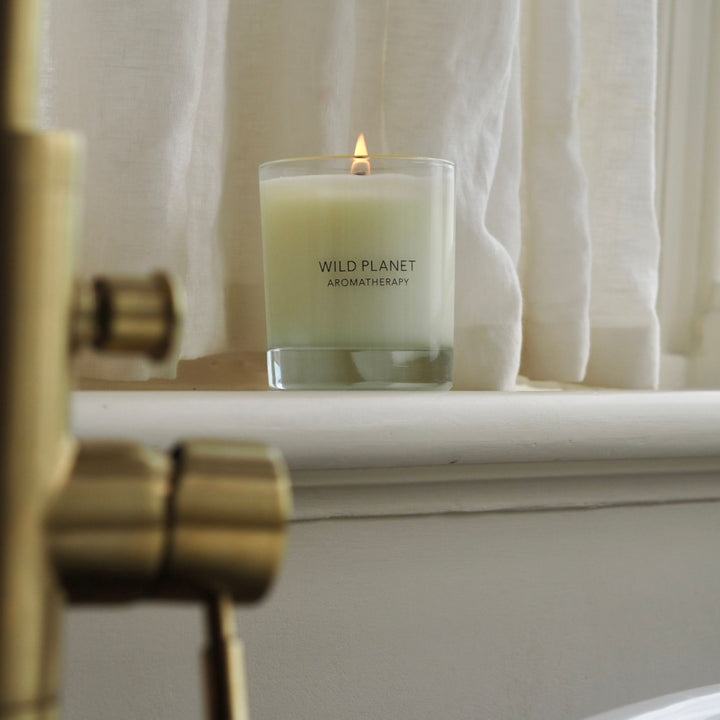 Wild Planet Aromatherapy vegan soy wax candle with essential oils burning on window sill by bath