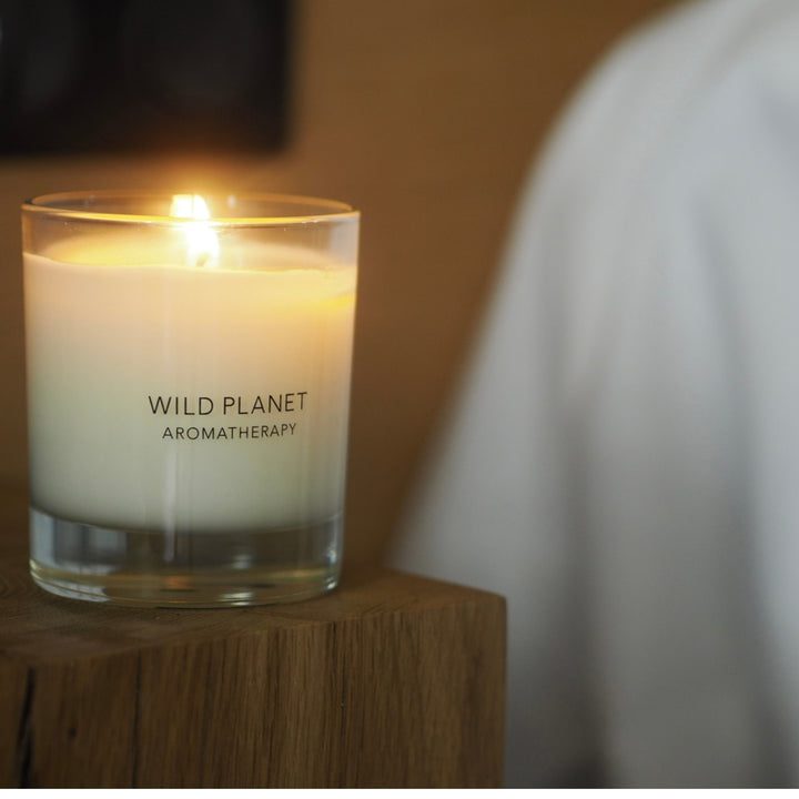 Wild Planet Aromatherapy calming natural candle lit on a wooden block with soft warm glow