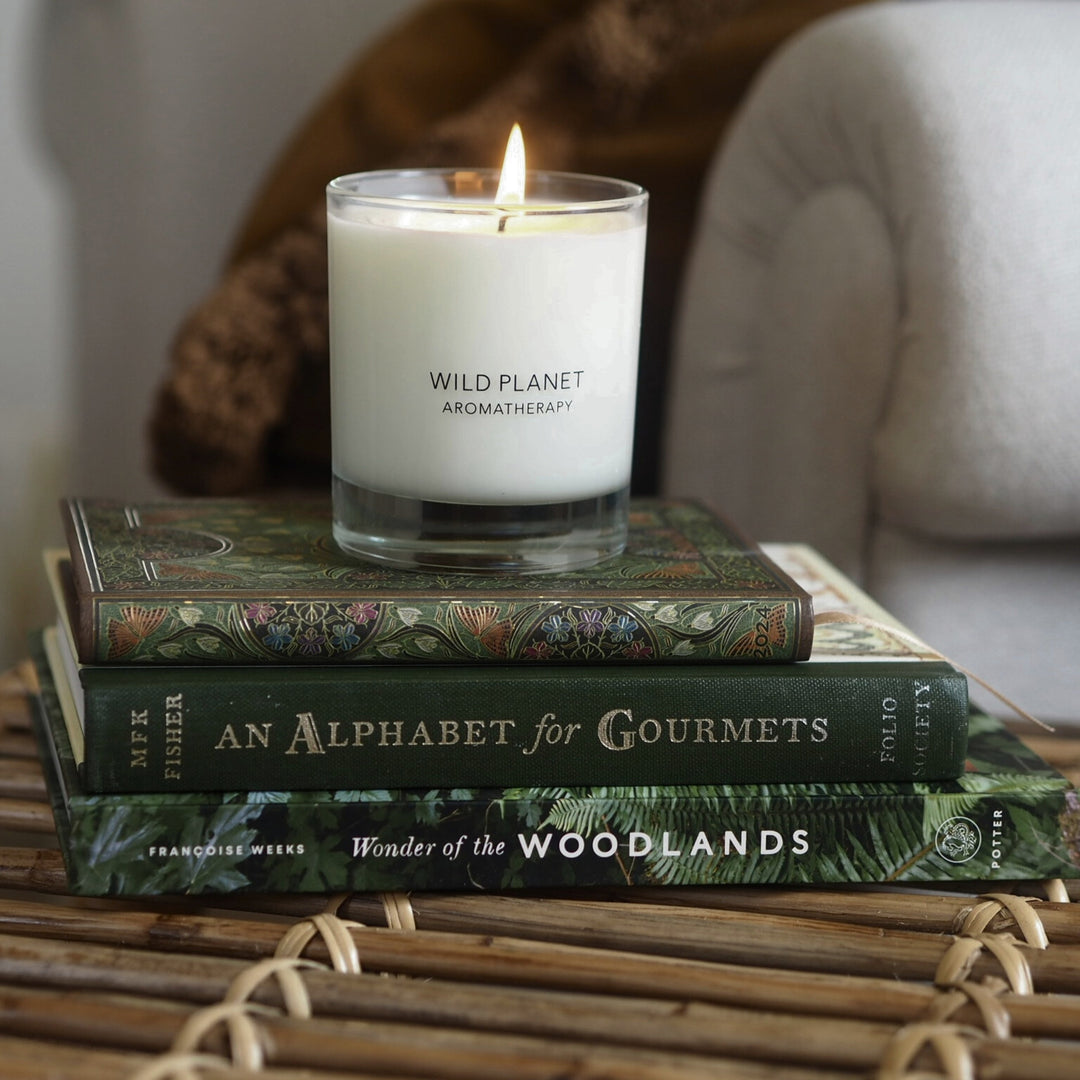 Wild Planet Aromatherapy vegan soy wax candle burning on top of stacked books on a wicker table