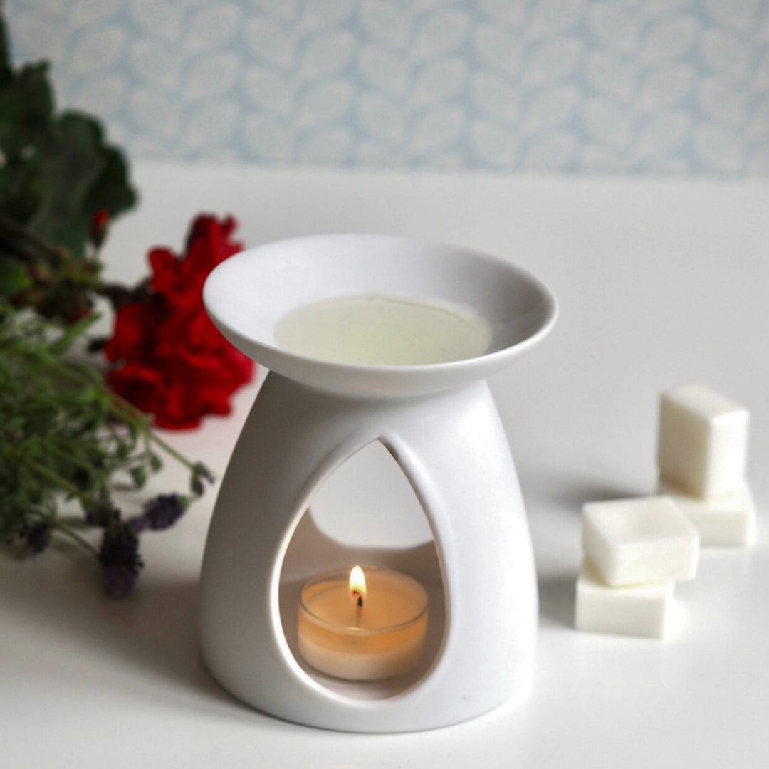 White ceramic oil burner with lit tea light heating Wild Planet luxury wax melts, next to red flower