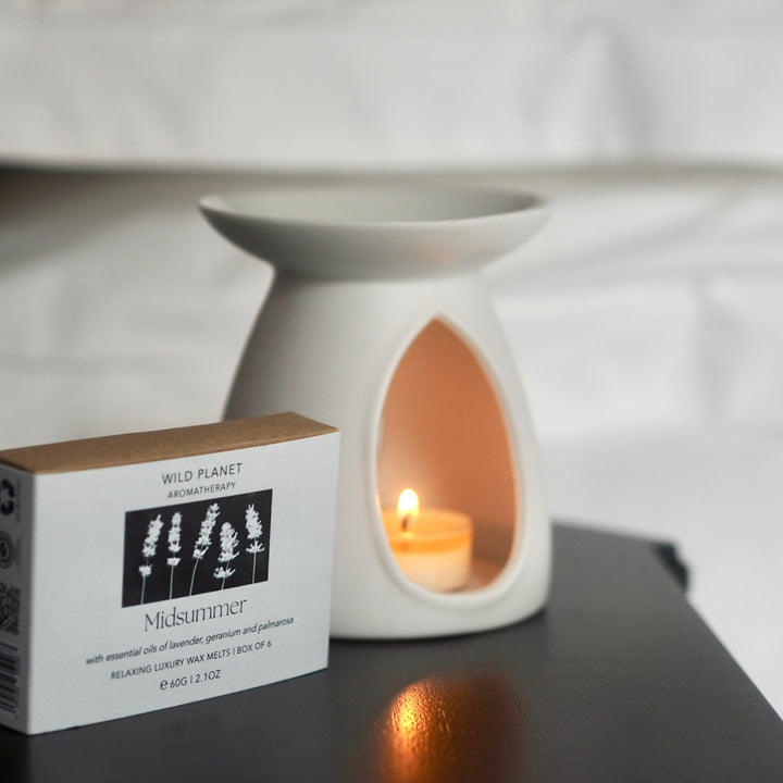 White ceramic oil burner with lit tea light heating Wild Planet luxury wax melts on wood table.