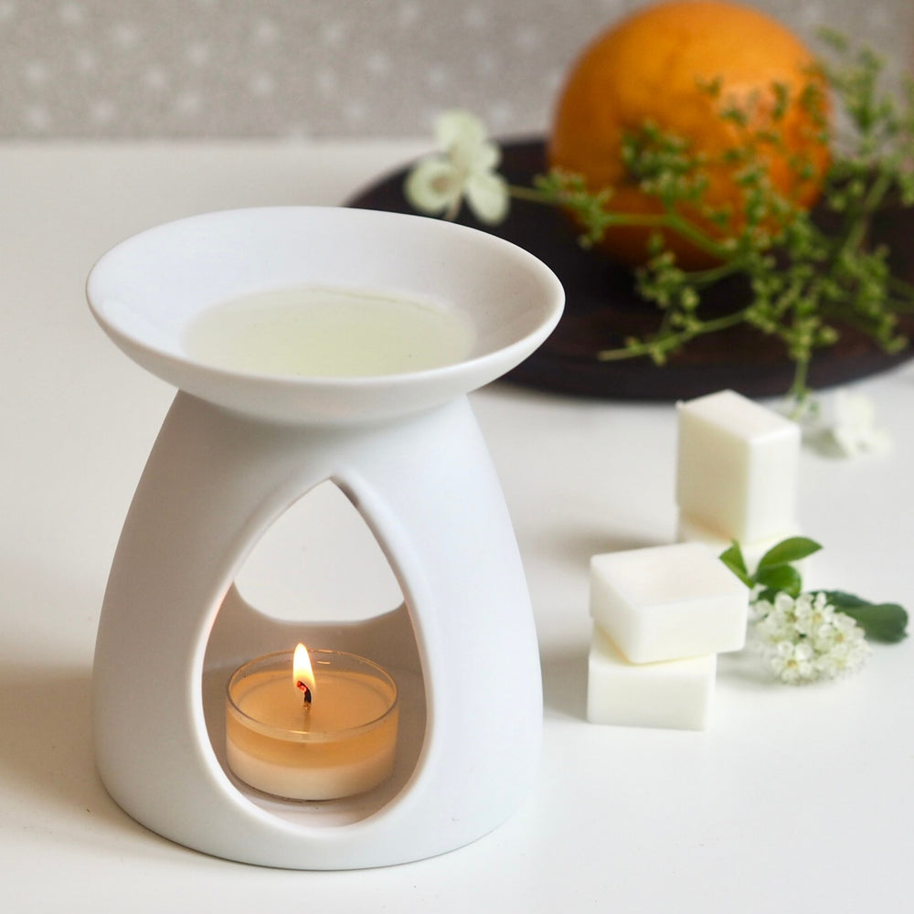 White ceramic oil burner, lit tea light heating Wild Planet luxury wax melt, orange in background