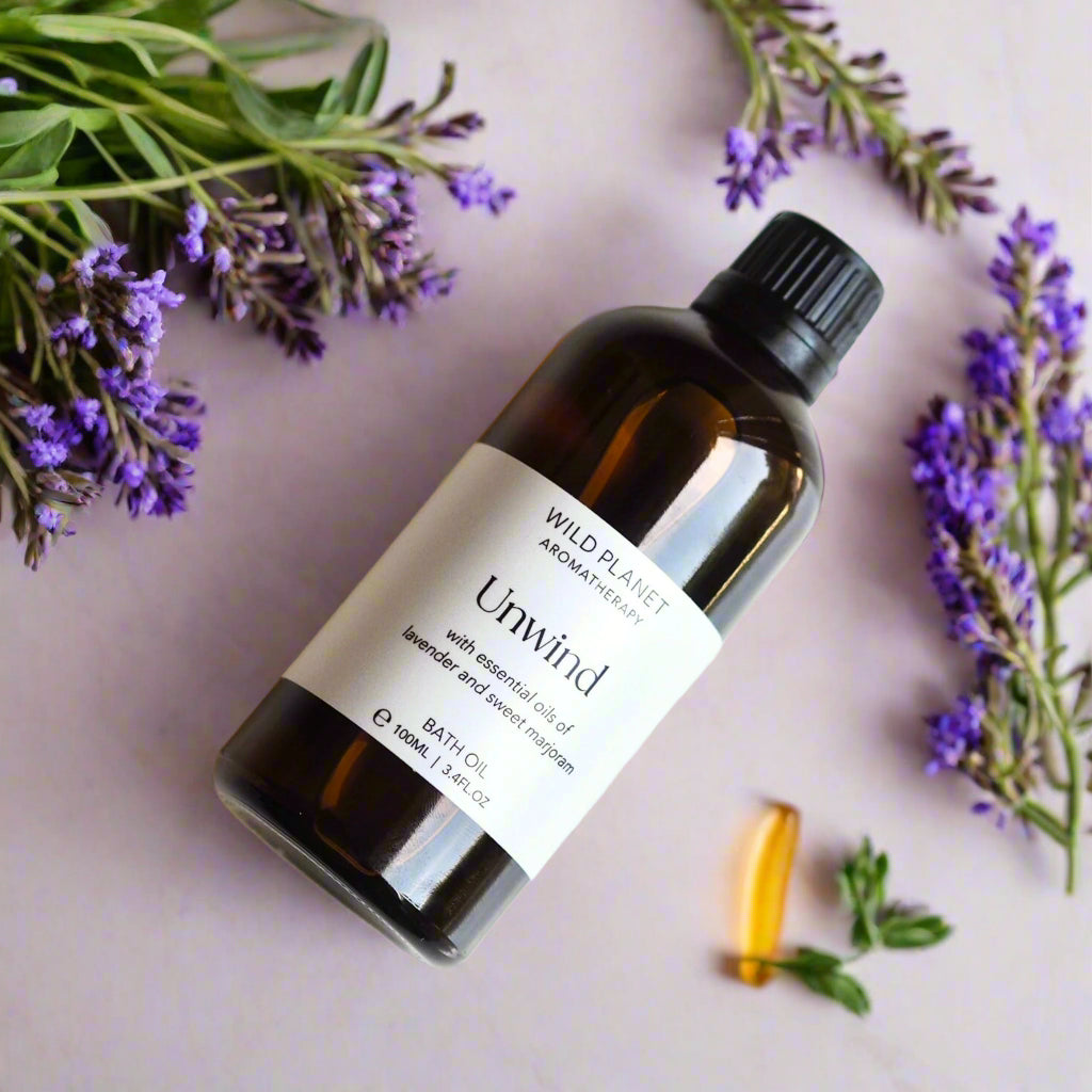 Unwind Natural Relaxing Lavender Bath Oil amber glass bottle flat lay image with lavender flowers