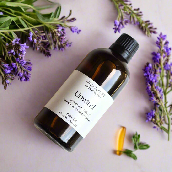 Unwind Natural Relaxing Lavender Bath Oil amber glass bottle flat lay image with lavender flowers
