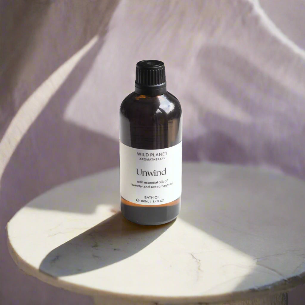 Unwind Natural Relaxing Lavender Bath Oil amber glass bottle, lilac background