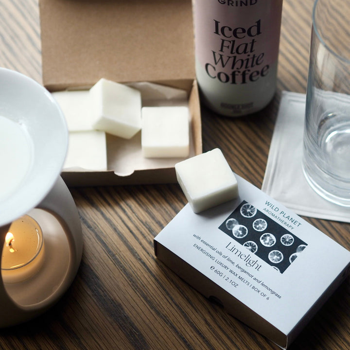 White ceramic oil burner with lit tea light heating Wild Planet luxury wax melts on wooden table.