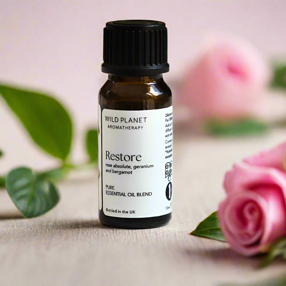 Essential oil bottle labeled 'Restore' by Wild Planet on a light background with roses and leaves
