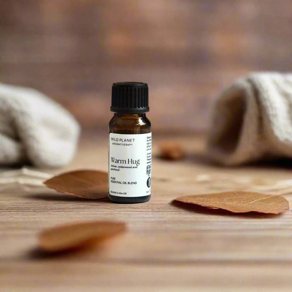Warm Hug comforting essential oil blend amber bottle on wooden table with dried leaves and blankets